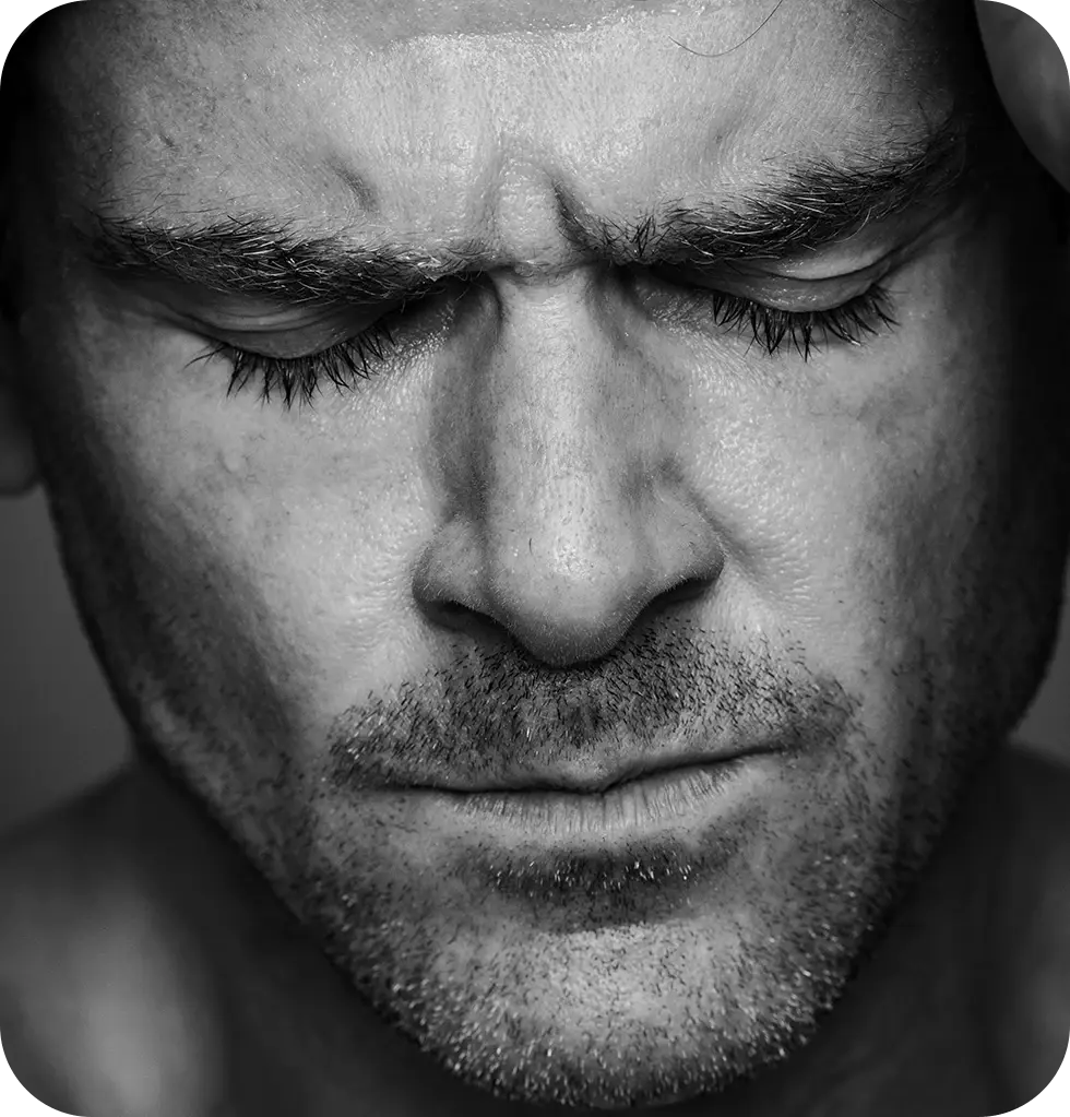 Close-up black-and-white portrait of a man with his eyes closed and brow furrowed, appearing tense