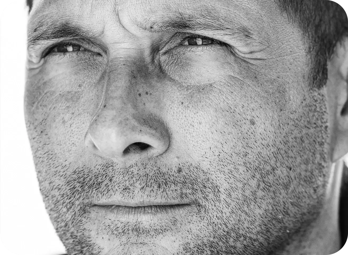Close-up black-and-white portrait of a man’s face showing detailed skin texture and an intense, focused expression.