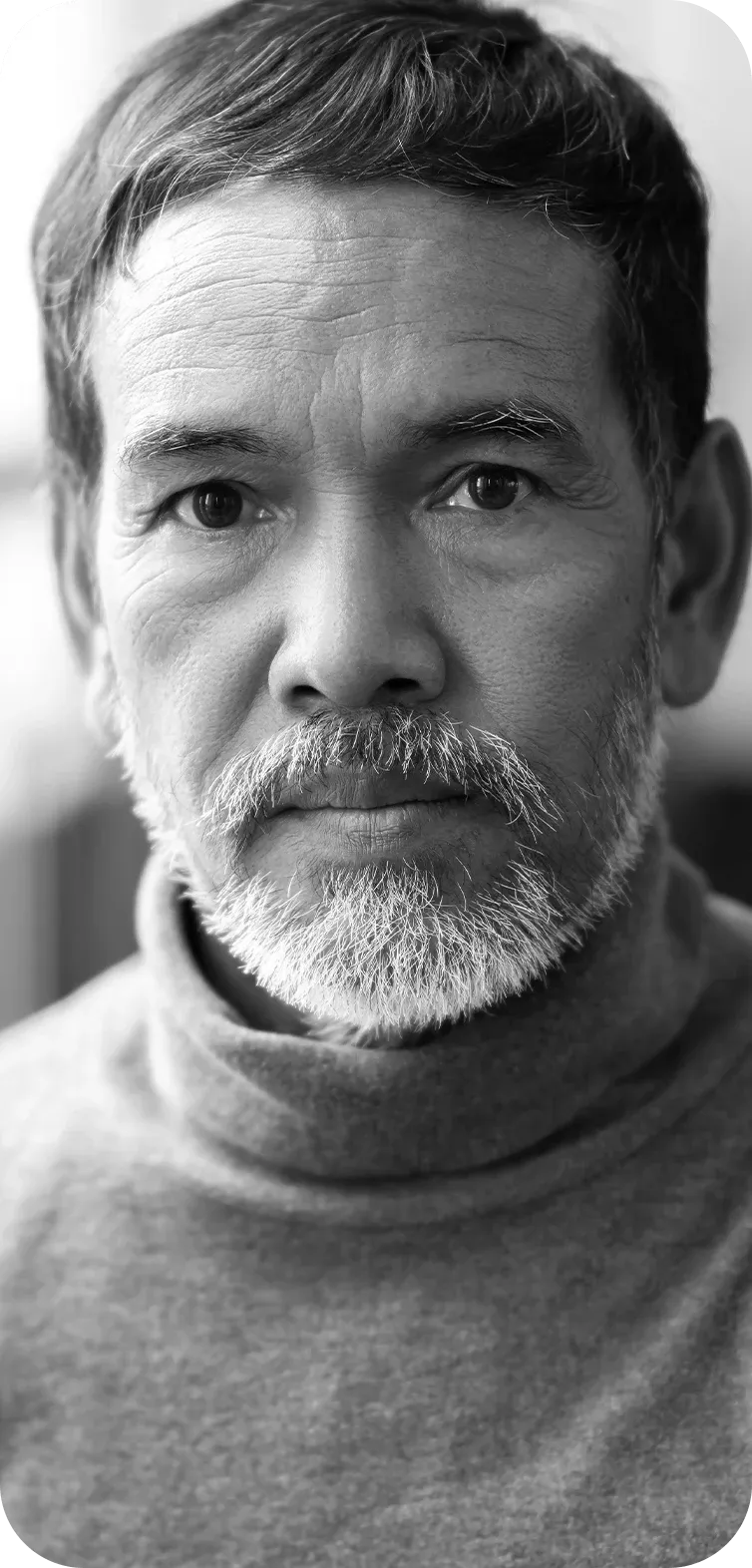 Black-and-white portrait of an older man with a short beard and mustache, looking directly at the camera while wearing a turtleneck sweater