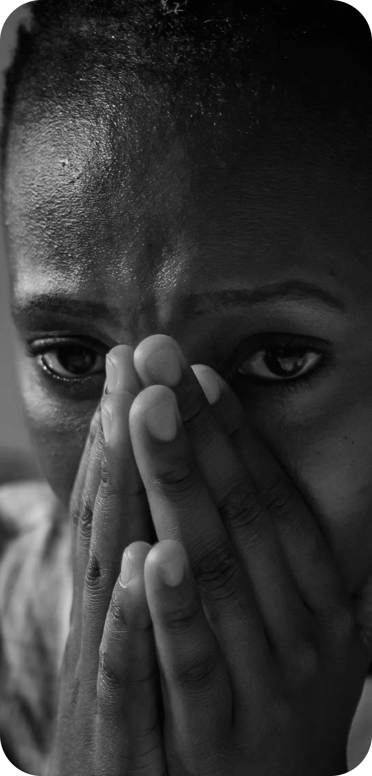 Black-and-white close-up of a person holding their hands over their mouth and nose, with wide, distressed eyes suggesting fear or anxiety